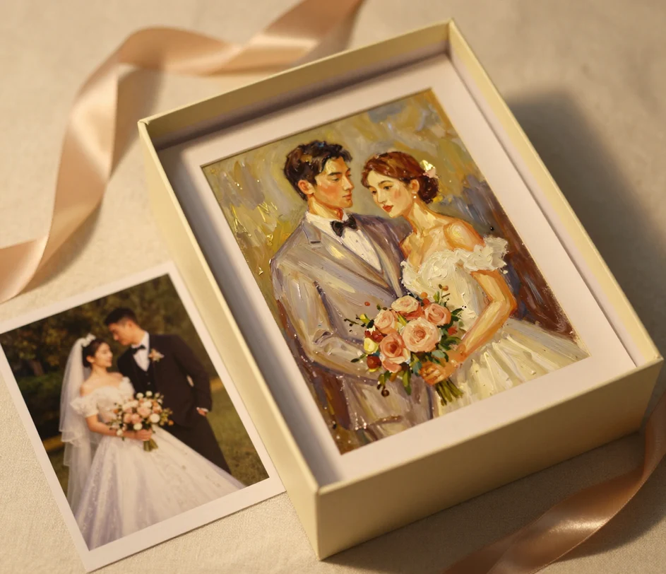A cream gift box with satin ribbon holding a framed oil-painting-style wedding portrait, with the original small photograph lying beside the box on the linen as a comparison